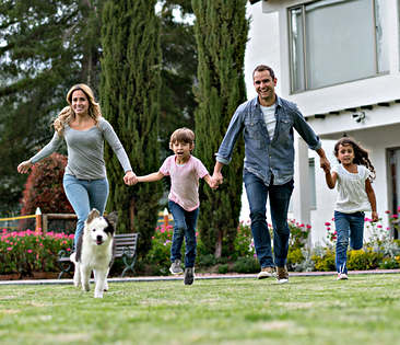 Wohngebäudeversicherung - Familie im Garten vor Hausfassade