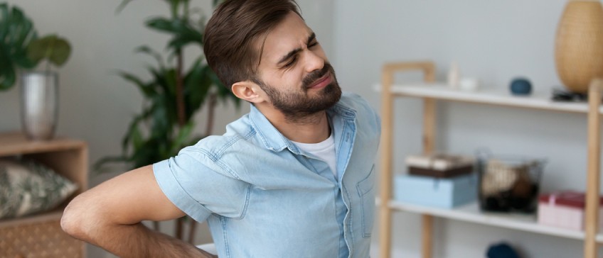 Ergonomisches Arbeiten - Mann hält sich schmerzenden Rücken