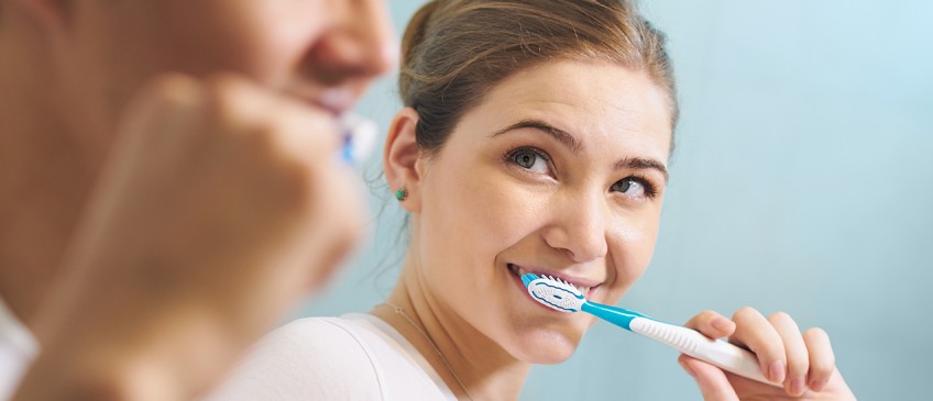 Zahnschutz - Frau lächelt Mann beim Zähneputzen an
