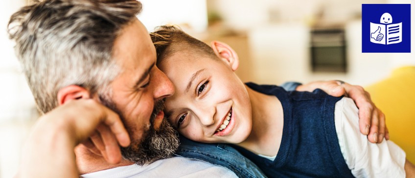 Leichte Sprache - Vater und Sohn sitzen Arm in Arm auf Sofa