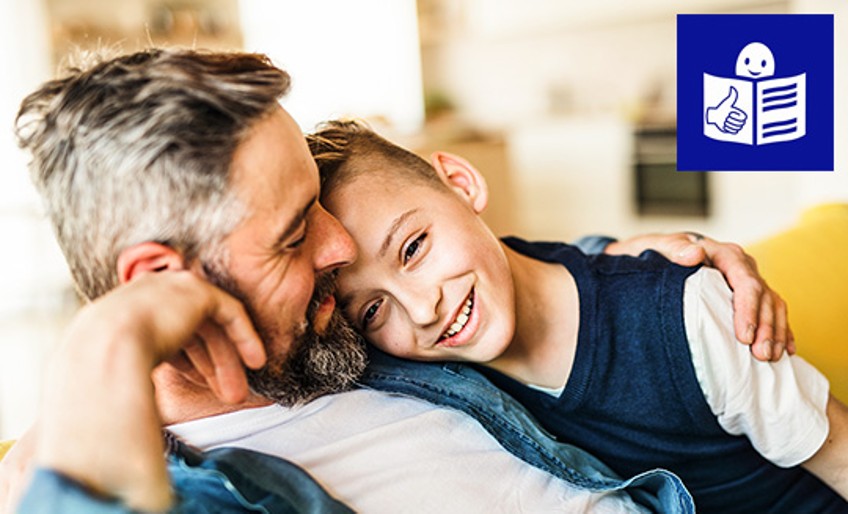 Leichte Sprache - Vater und Sohn sitzen Arm in Arm auf Sofa