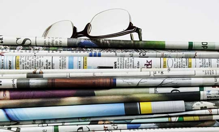 Newsfeed - Lesebrille liegt auf Zeitungsstapel
