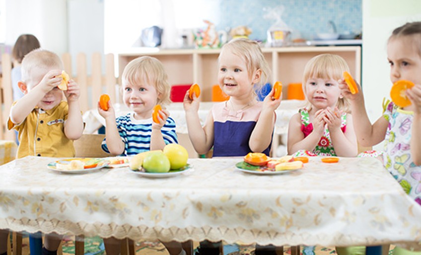 Ratgeber Kita-Anspruch - Kindergartenkinder halten Obstscheiben hoch