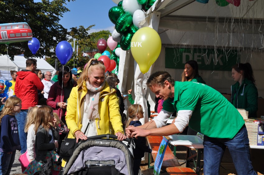 Pressemitteilung Weltkindertag - Mitarbeiter bindet Luftballon an Kinderwagen