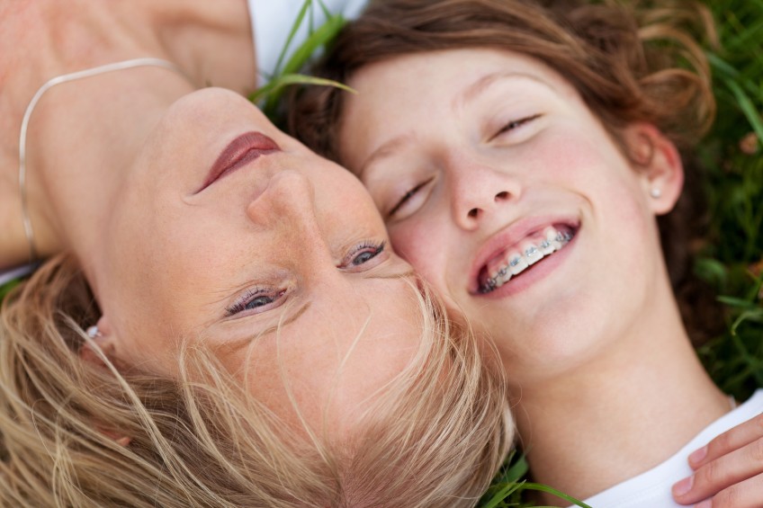 Pressemitteilung Zahnpangen für Kinder: Mutter und Tochter mit Zahnspange im Gras